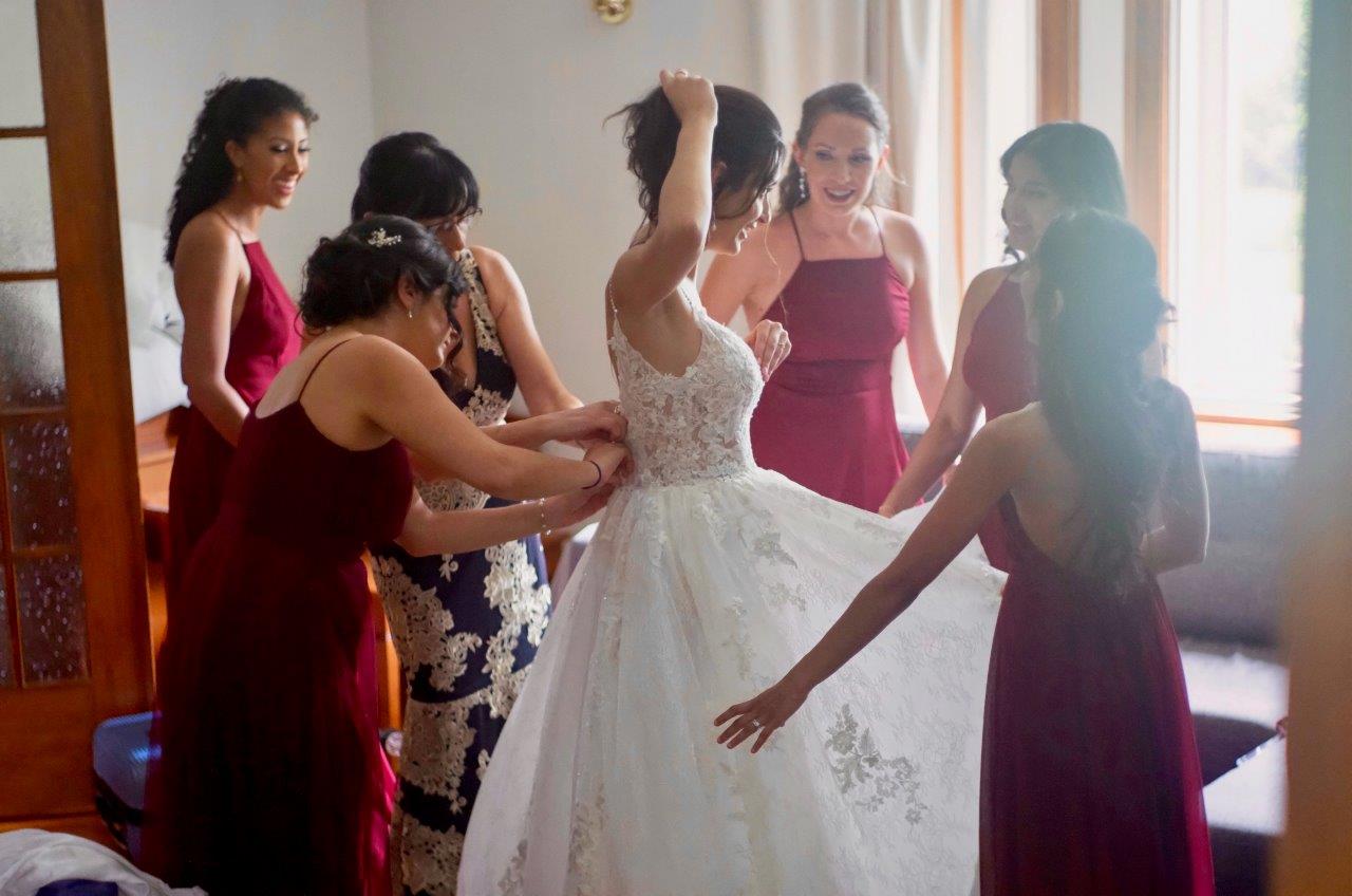 evermore weddings bridesmaids helping to put dress on bride